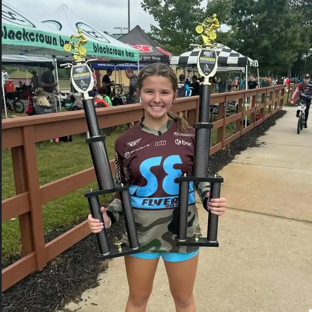 BMX Racer holding up two trophies from BML Trophies